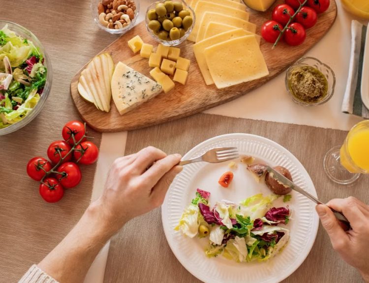 Overhead view of a cheese platter with fresh salad and juice, perfect for a gourmet lunch setting.